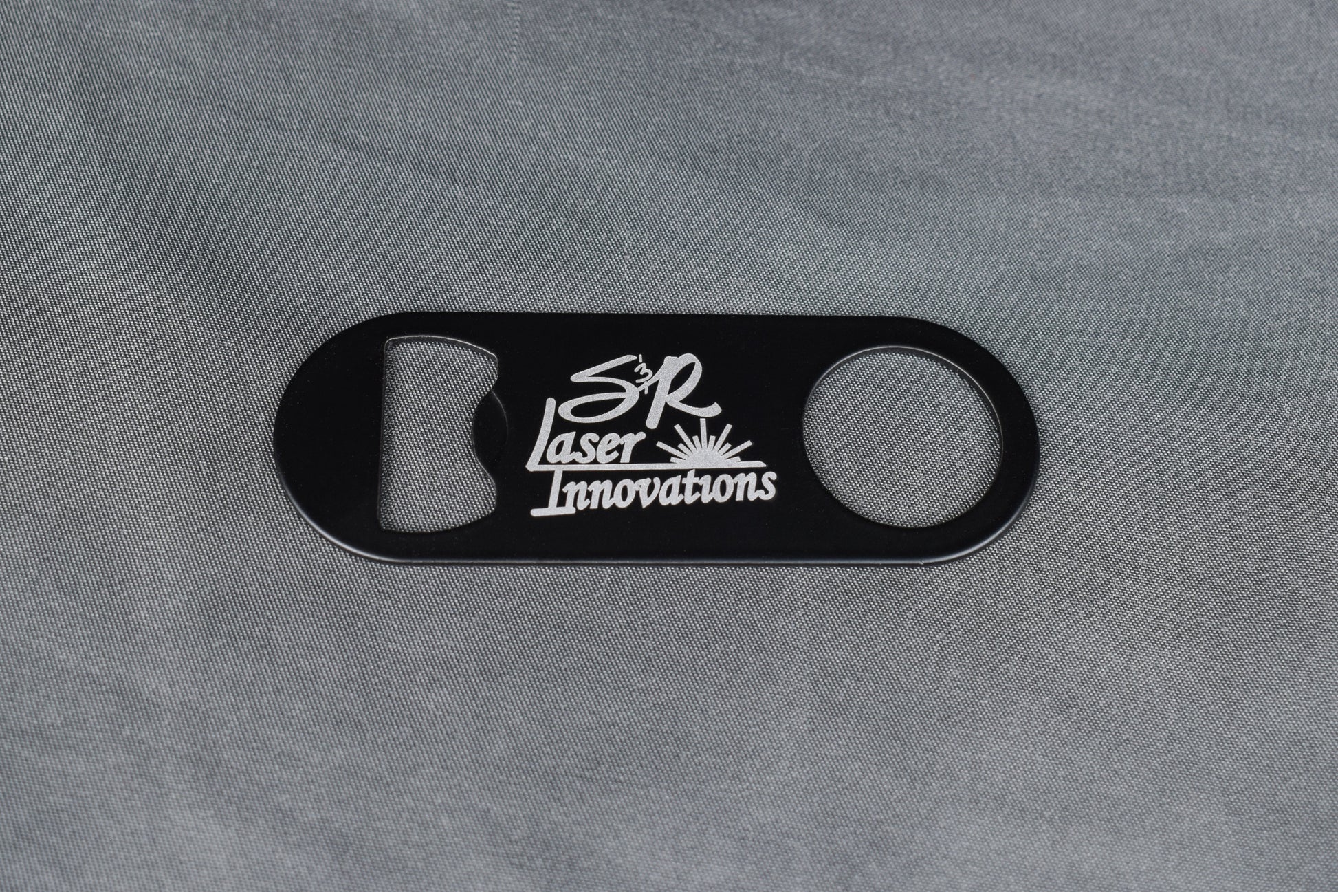 Black bottle opener with white logo on gray background